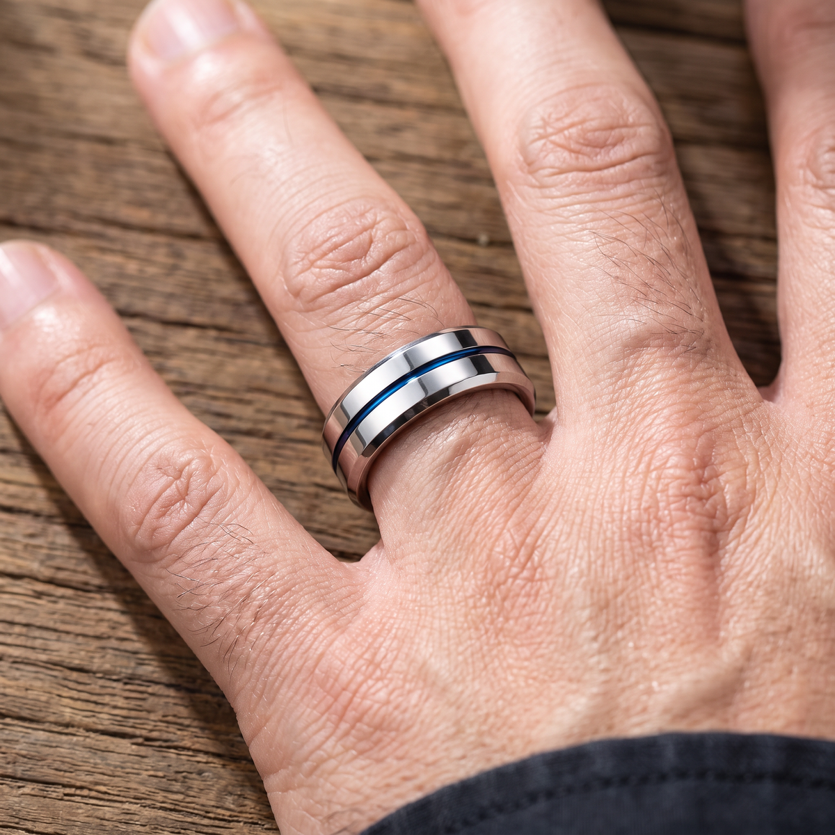Close up of a man's hand wearing The Meridian tungsten ring with a blue groove line