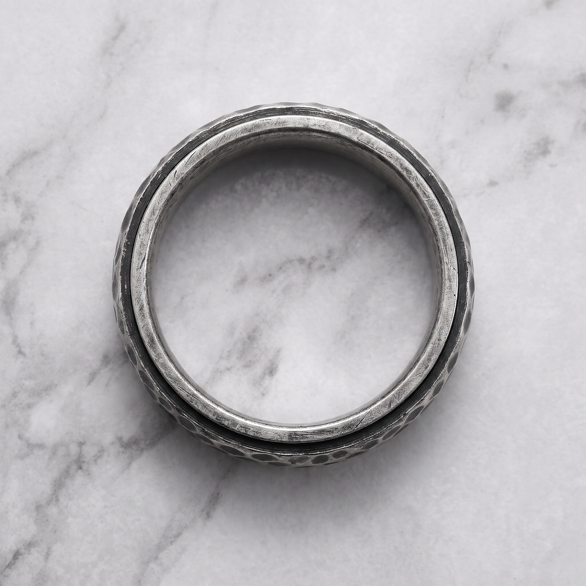 The Crater antique hammered ring lying flat on a light grey marble surface