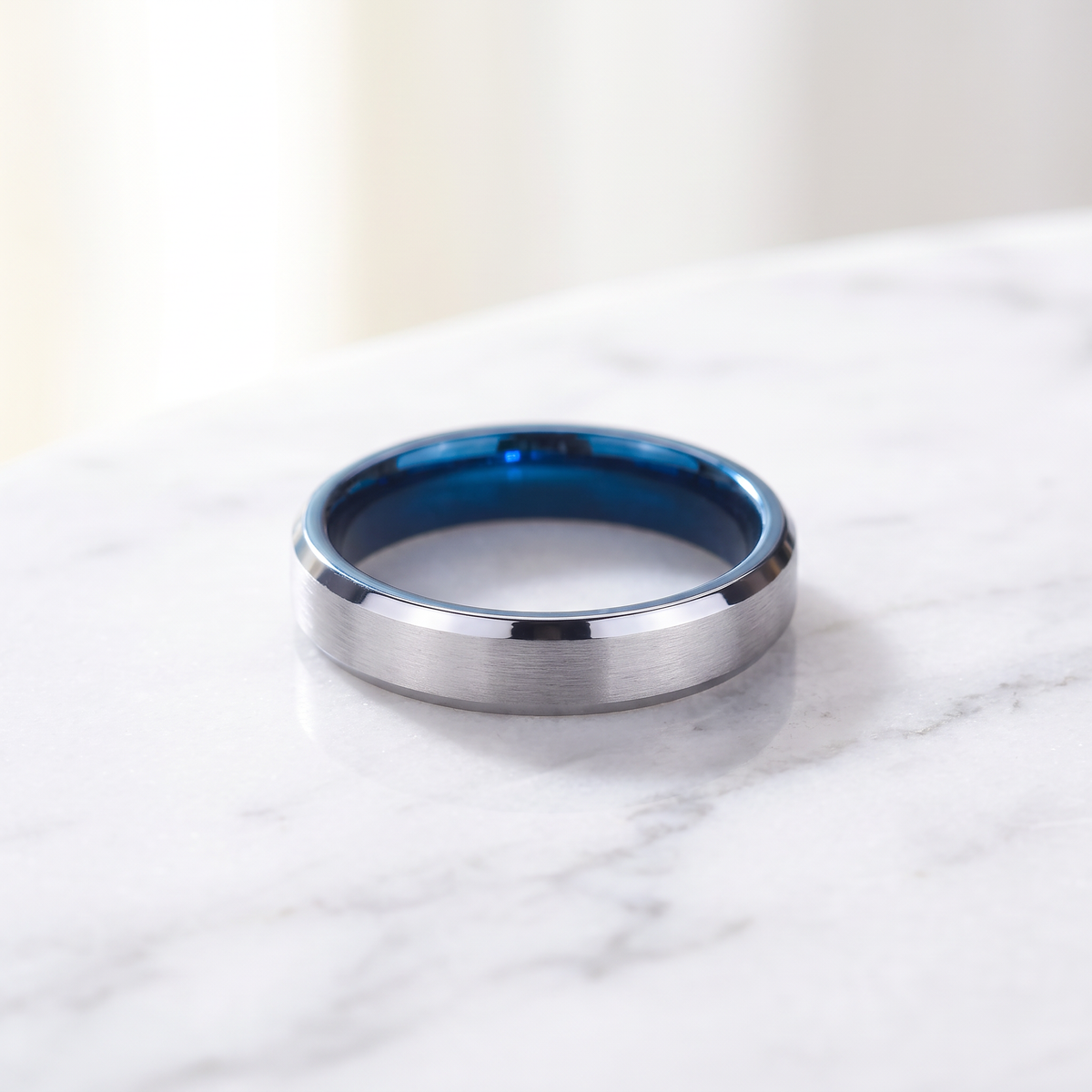 The Halcyon slim silver tungsten ring with a blue inside lying flat on white marble