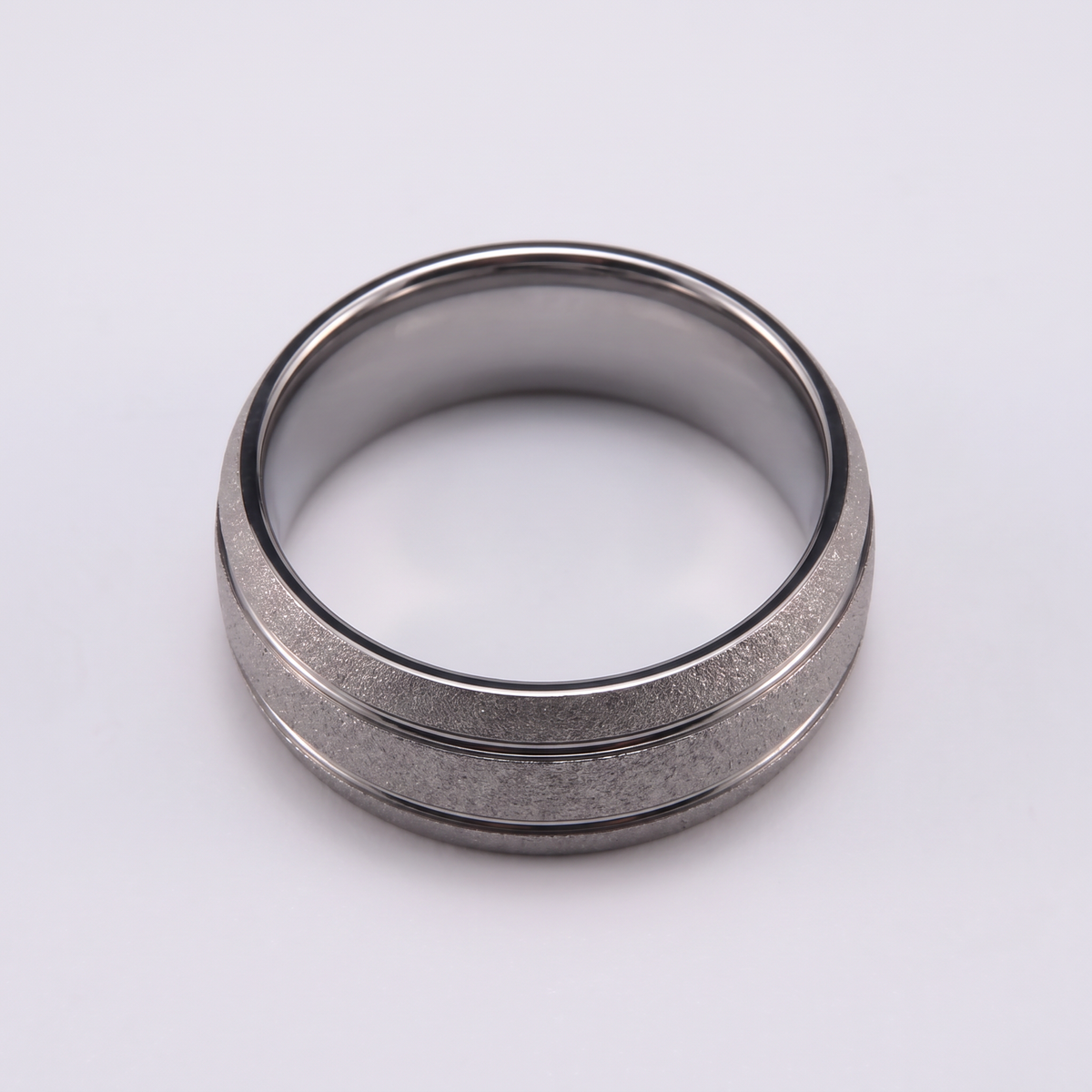 The Granite silver sandblasted tungsten ring lying flat on a light grey surface