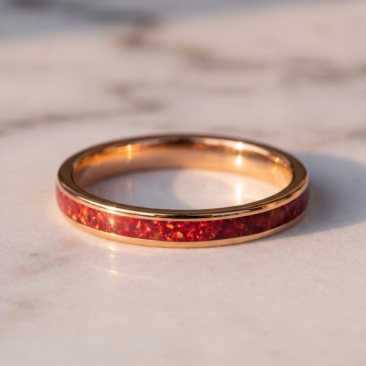 The Cinder rose color tungsten ring with a red opal inlay lying flat on a marble surface