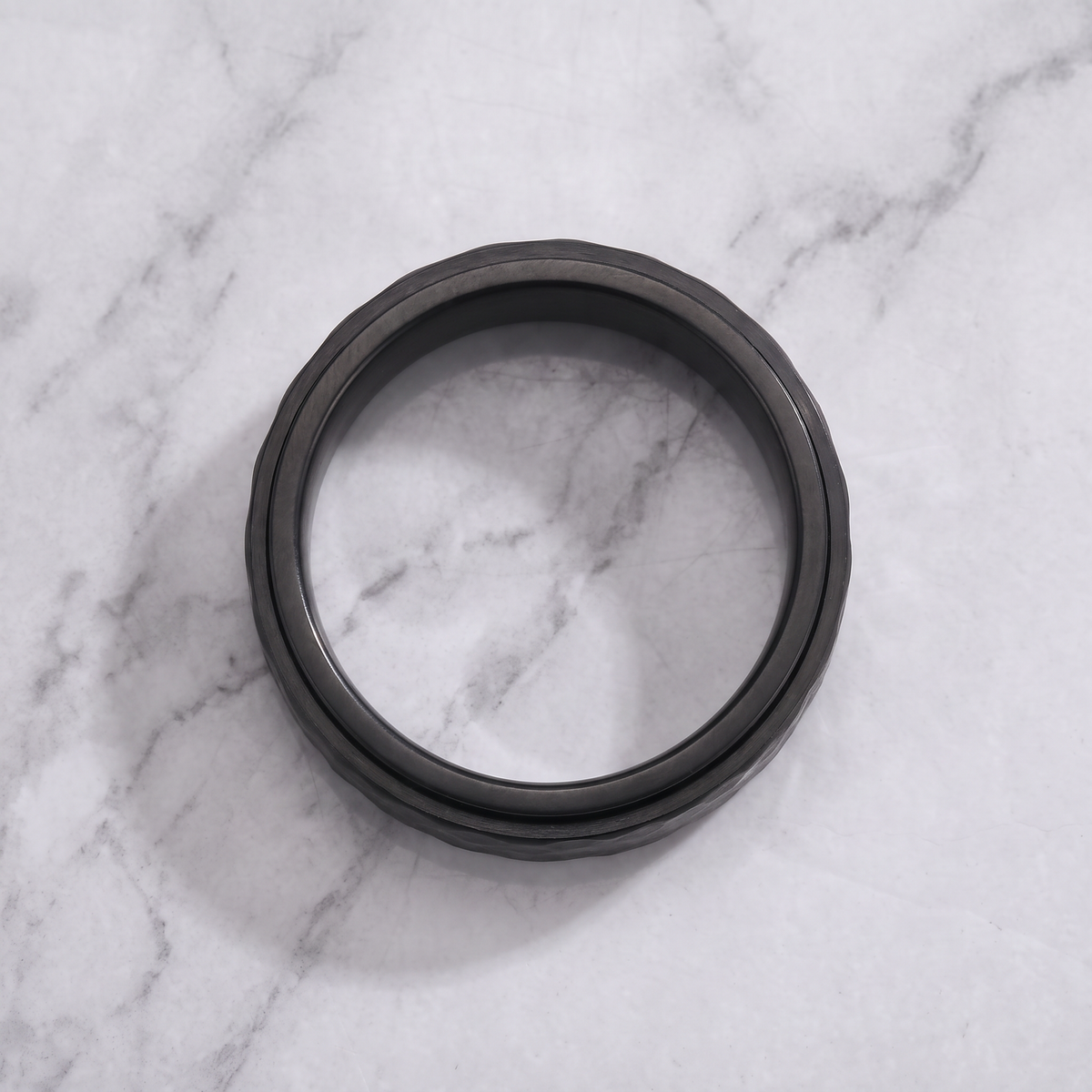 The Orbit black spinner ring lying flat on a light grey marble surface