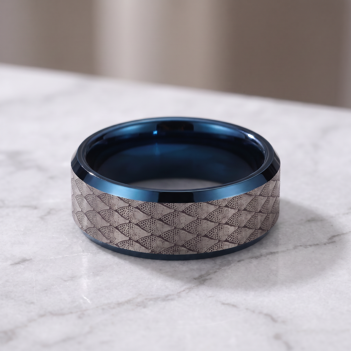 The Serpentine tungsten ring with a blue interior lying flat on a light grey marble surface