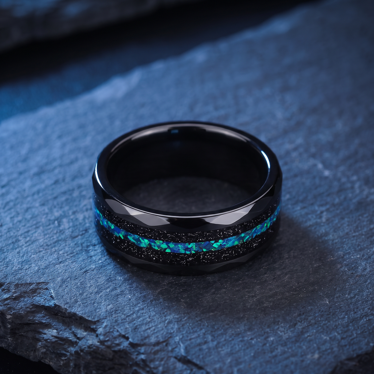 The Reef black tungsten ring with black sand and green blue opal inlay lying flat on dark slate