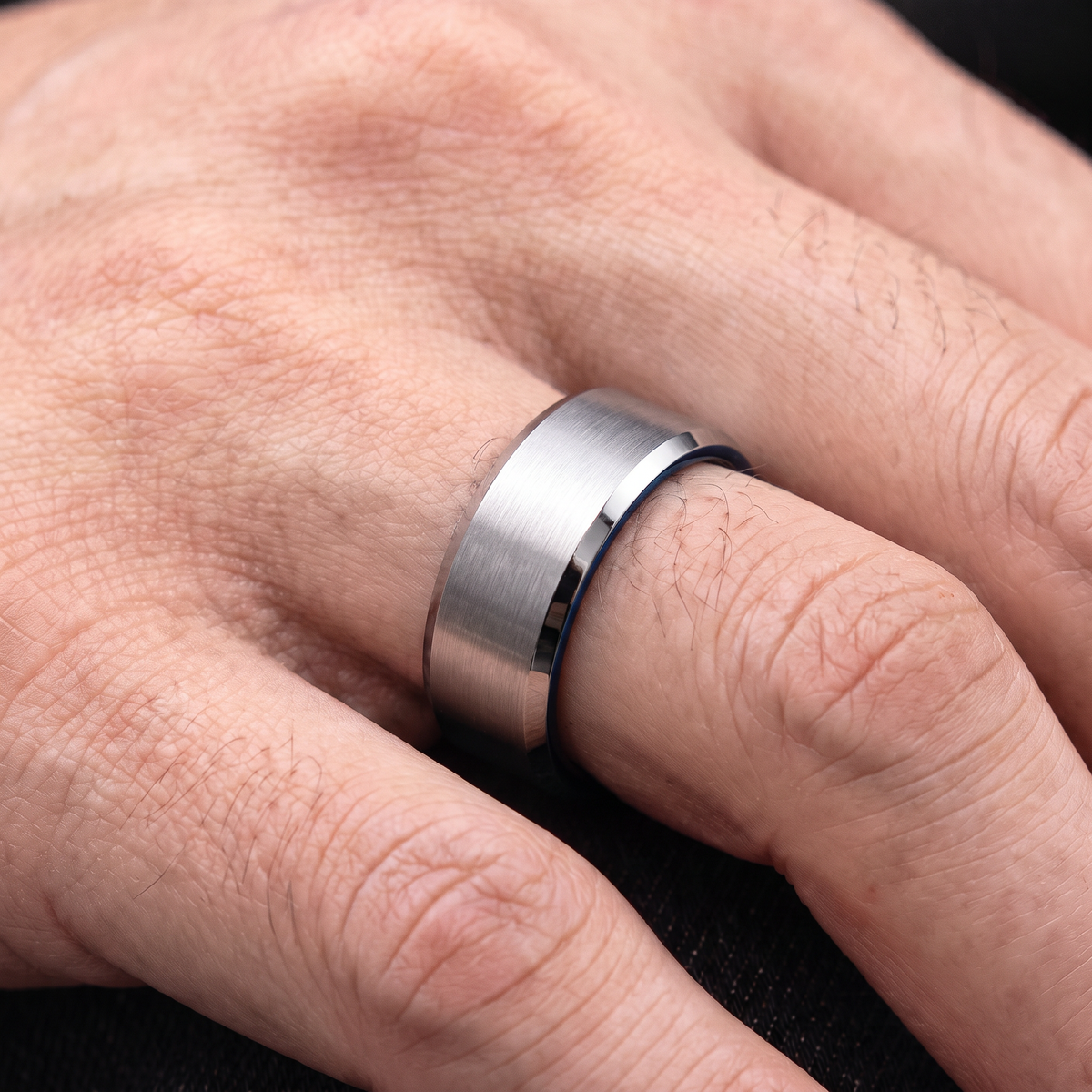 Close up of a man's hand wearing The Fathom 8mm silver tungsten ring with a blue inside
