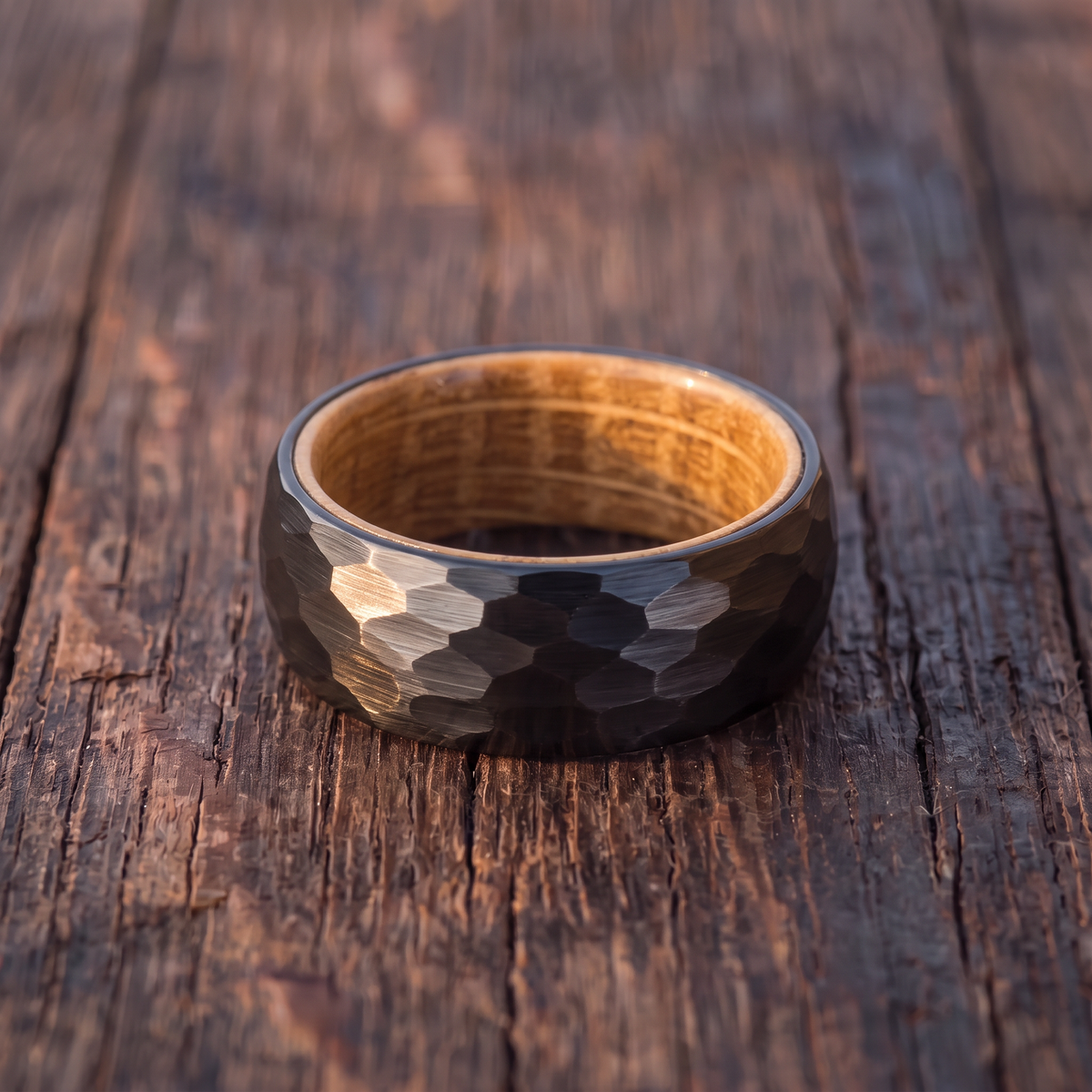 The Cask black hammered tungsten ring with a whiskey barrel wood interior lying flat on weathered dark oak