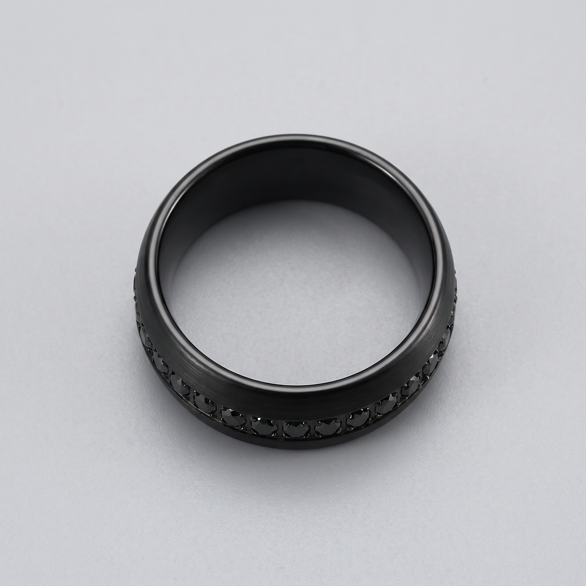 The Obsidian black brushed tungsten ring with black CZ stones lying flat on a light grey surface