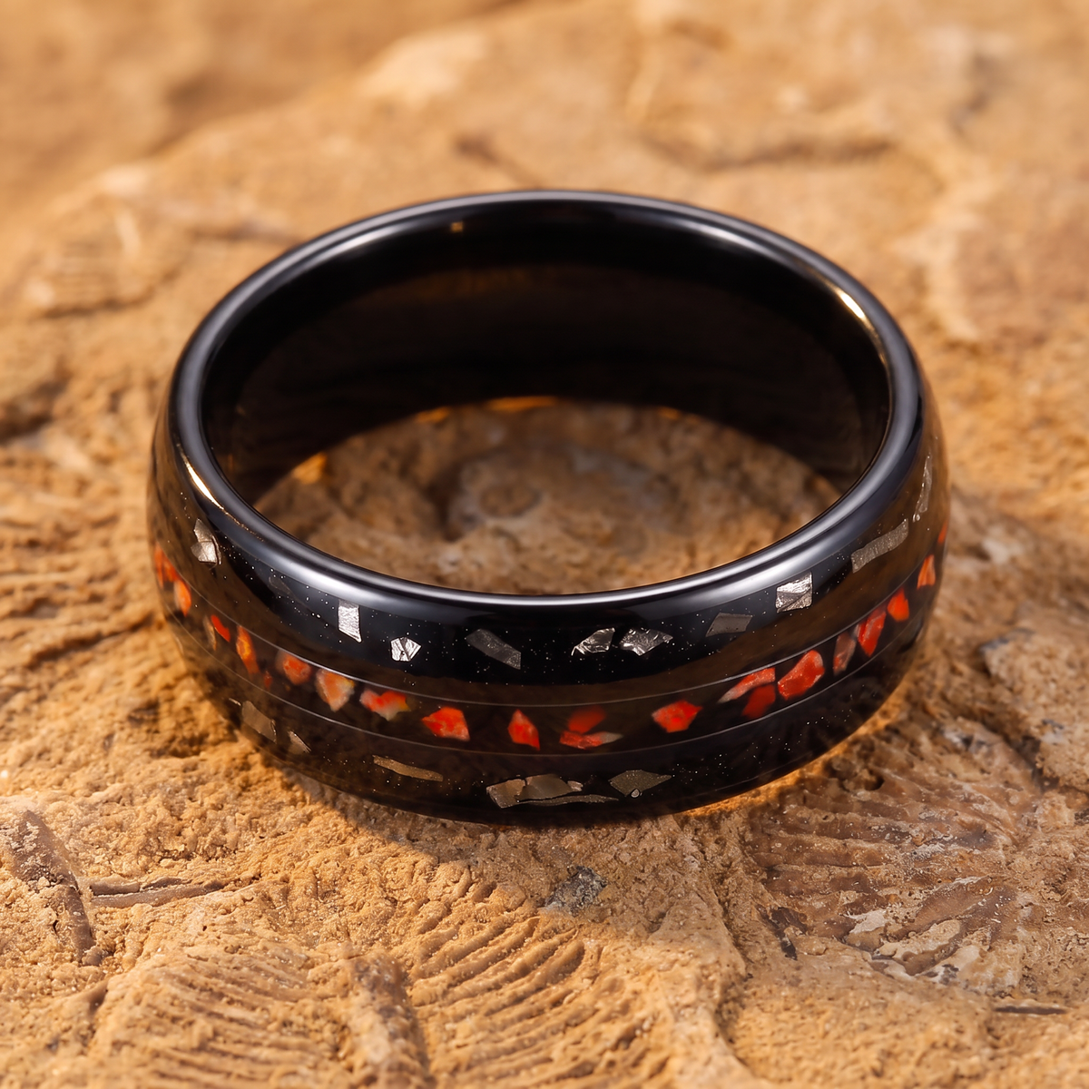 Domed black tungsten ring with dinosaur bone inlay lying flat on a fossil rock slab