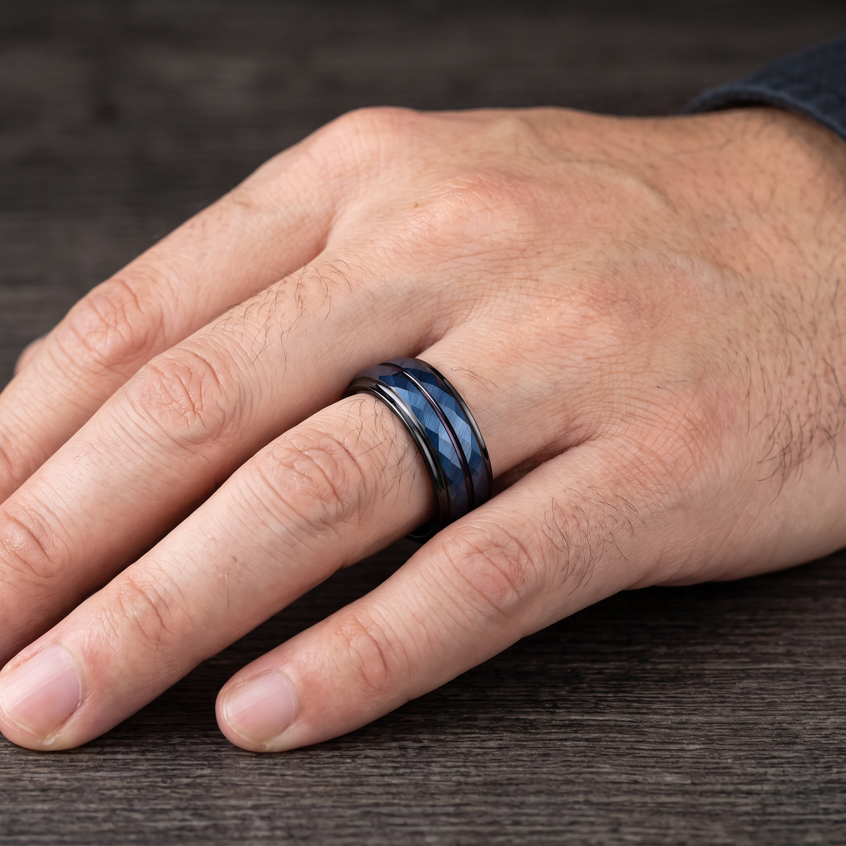 Close up of a man's hand wearing The Lattice black tungsten ring with a blue rhombus cut face