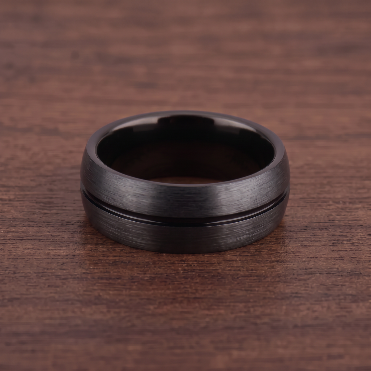The Furrow black brushed tungsten ring with a groove lying flat on dark walnut wood