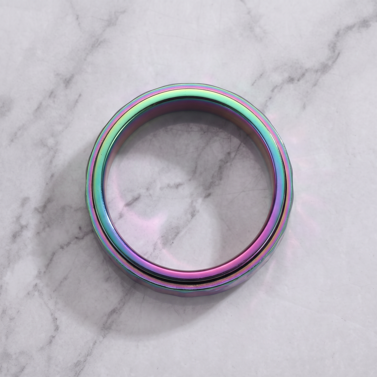 The Orbit rainbow spinner ring lying flat on a light grey marble surface