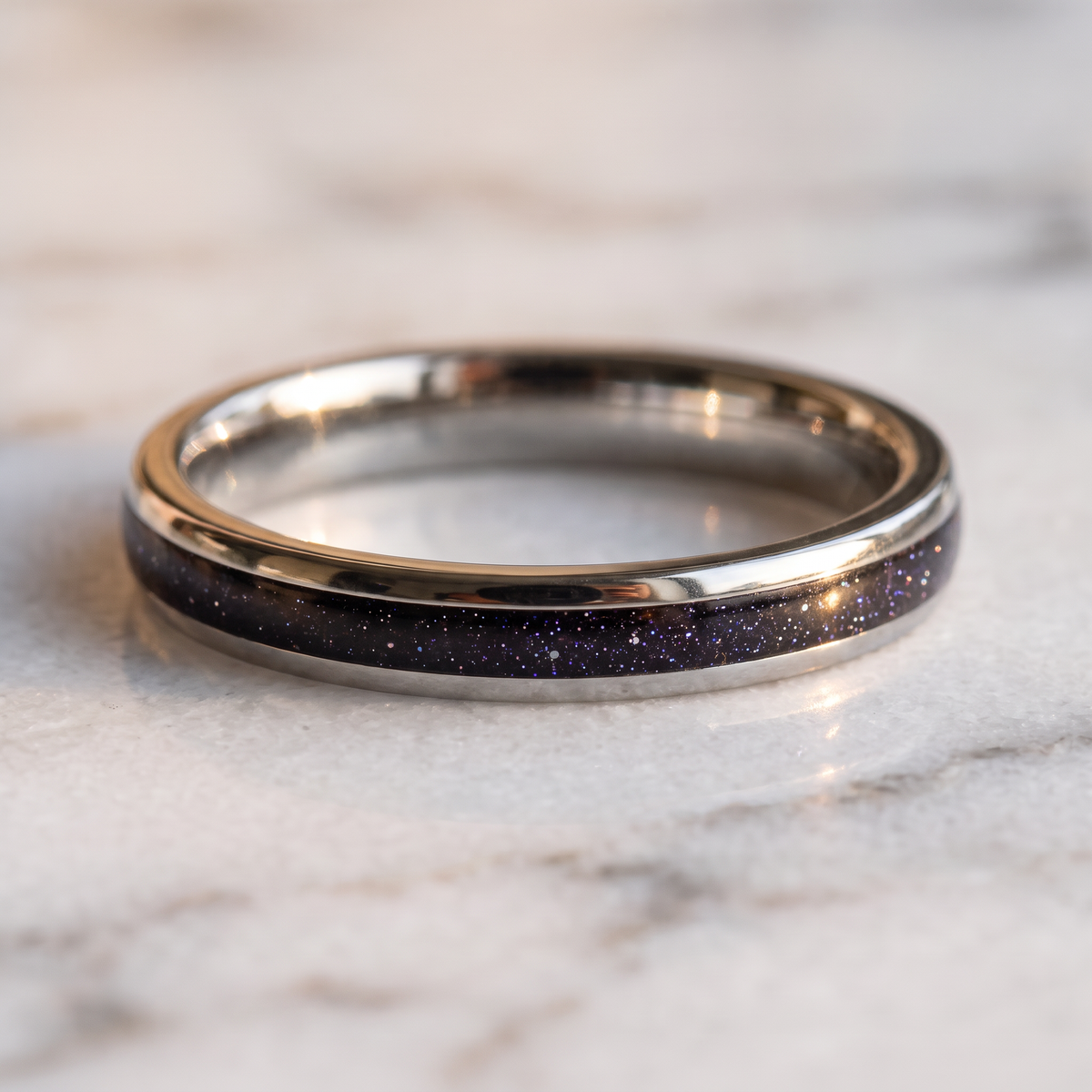 The Vega silver color tungsten ring with a galaxy opal inlay lying flat on a marble surface