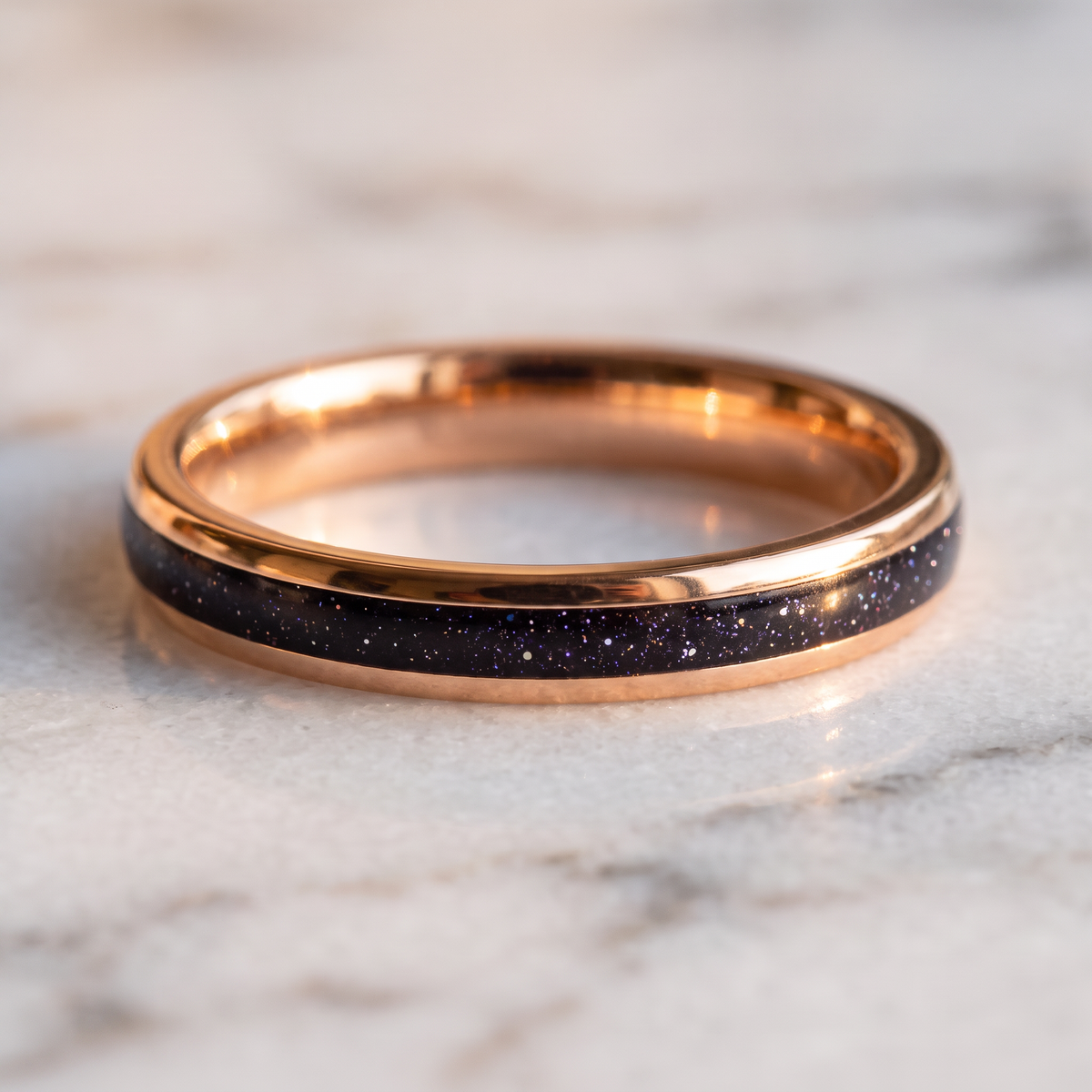 The Vega rose color tungsten ring with a galaxy opal inlay lying flat on a marble surface